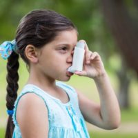Little girl using her asthma inhaler on a sunny day
